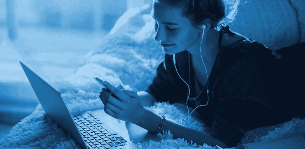 Joven con auriculares escuchando radio desde el celular junto a su notebook